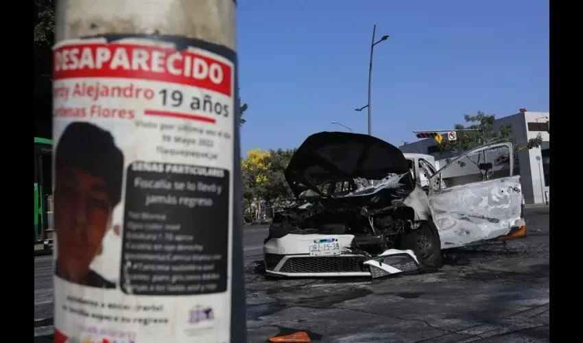 Fotografía que muestra un cartel de una persona desaparecida y un vehículo incendiado, este 22 de febrero de 2026, en una vía de Guadalajara (México). EFE/ Francisco Guasco